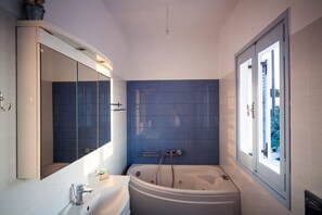 A modern bathroom with a bathtub, a sink, and a large mirror. - Luna Rossa (Santorini)