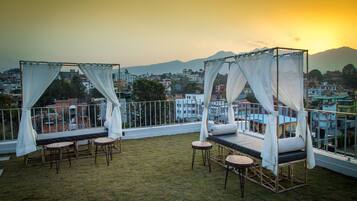 A balcony with a bed and seating area, overlooking a cityscape and mountains.