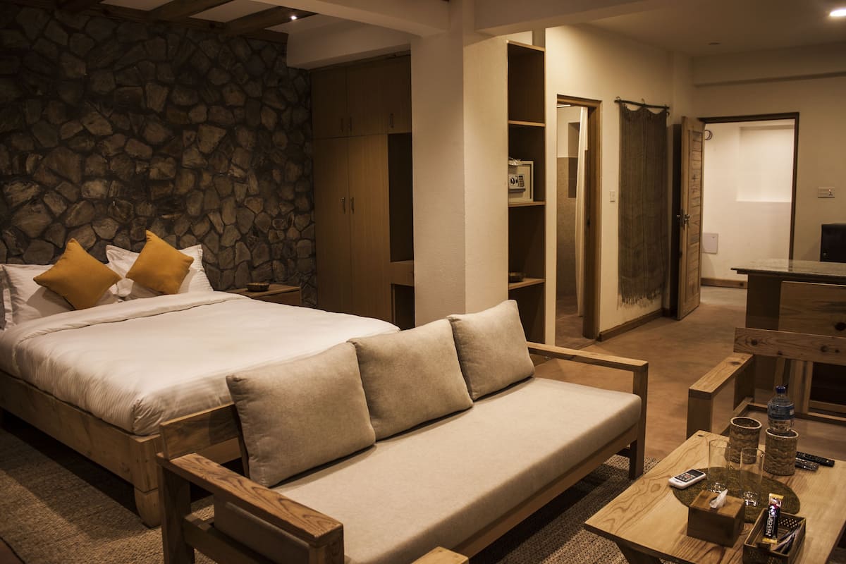 Un dormitorio con cama, un banco de madera, una mesita con una botella y una pared de piedra.