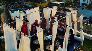 Terraza en la azotea con mesas y sillas, rodeada de cortinas blancas.