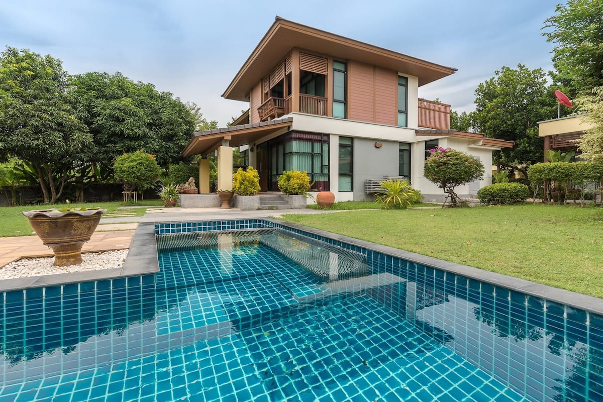 A modern two-story house with a swimming pool, surrounded by well-maintained lawns and various plants.