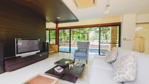 A modern living room with a flat-screen TV, a sofa, a coffee table, and a patterned armchair. - Pool Villa Pattaya by Passionata (Pattaya)