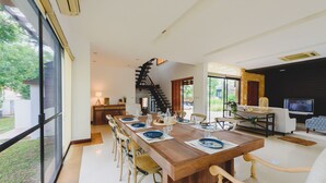 A modern dining area with a wooden table set for six, surrounded by chairs. A staircase leads to an upper level. - Pool Villa Pattaya by Passionata (Pattaya)