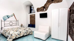 Un dormitorio con una cama, una silla blanca, un armario y una pared de piedra.