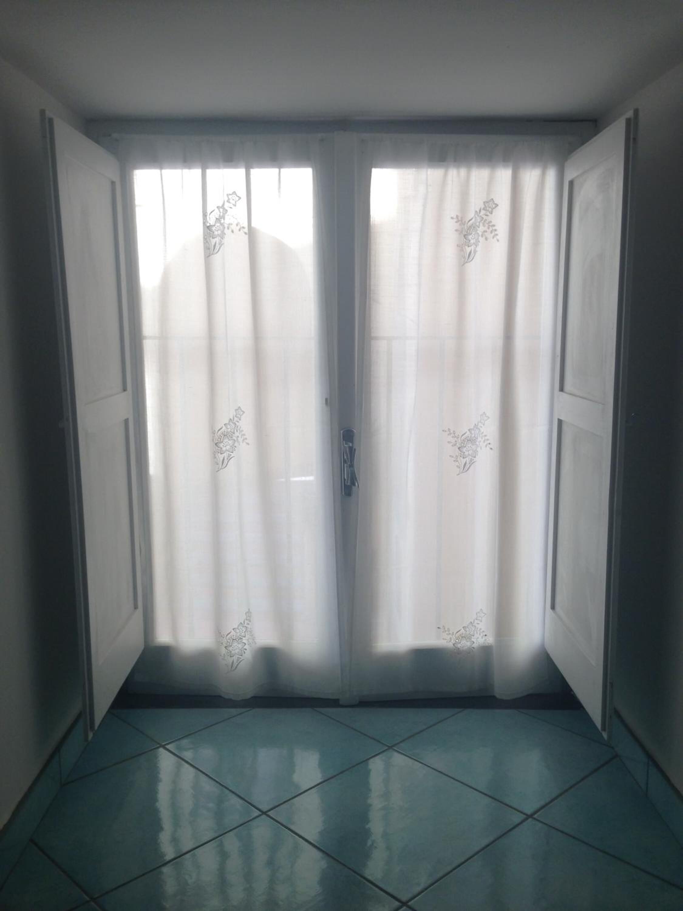 Ein Zimmer mit Fliesenboden und doppelt verglasten Glastüren mit floralen Vorhängen.