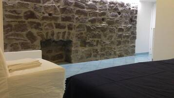 A room with a stone wall, a bed, a chair, and a small fireplace.