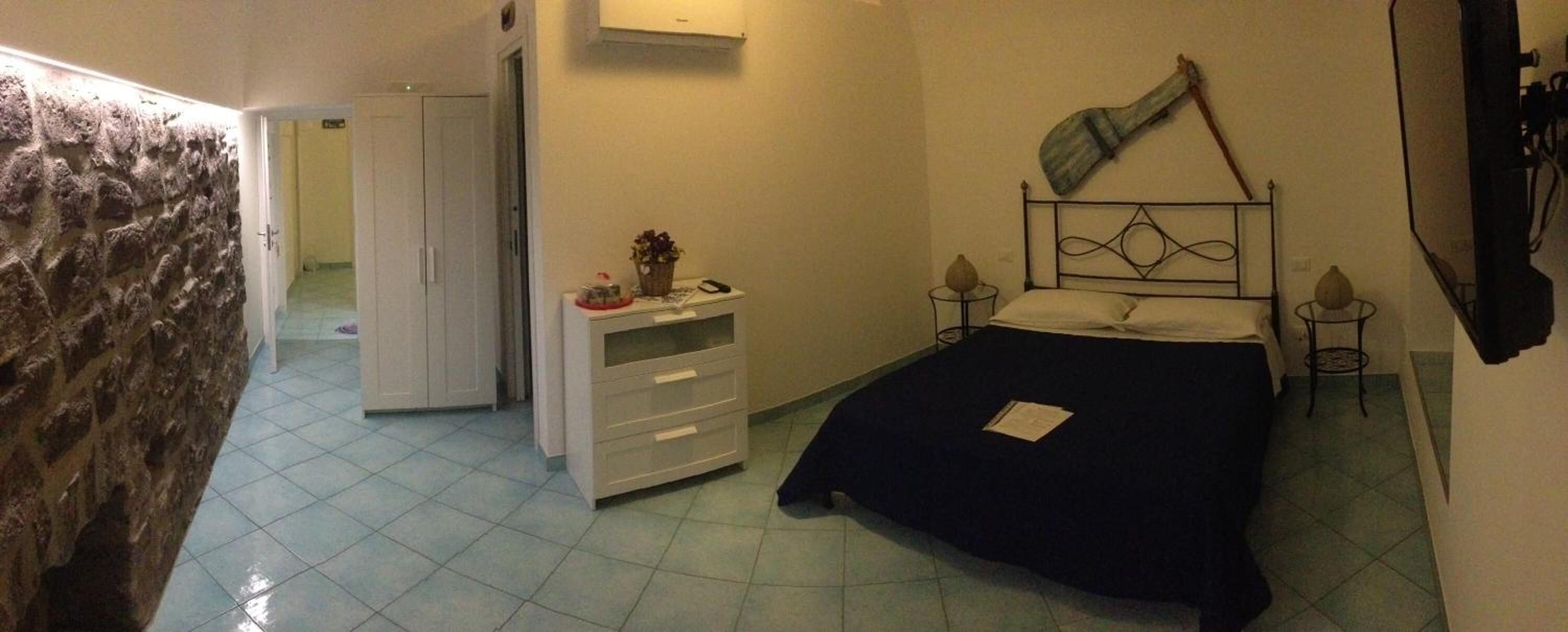 Un dormitorio con una cama, un aparador, un espejo y una guitarra en la pared.