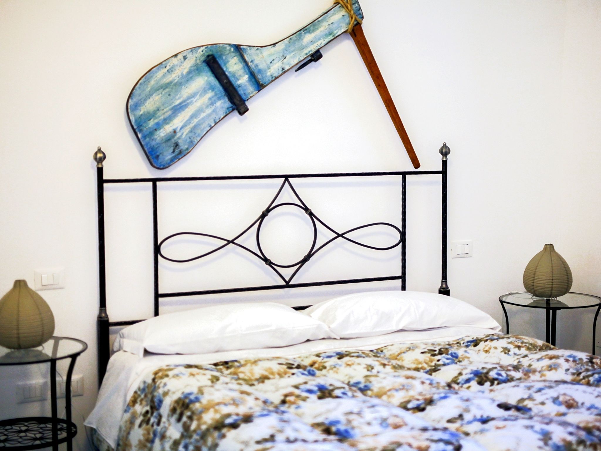 A bed with a floral bedspread, a metal headboard with a decorative design, and two bedside tables with vases.