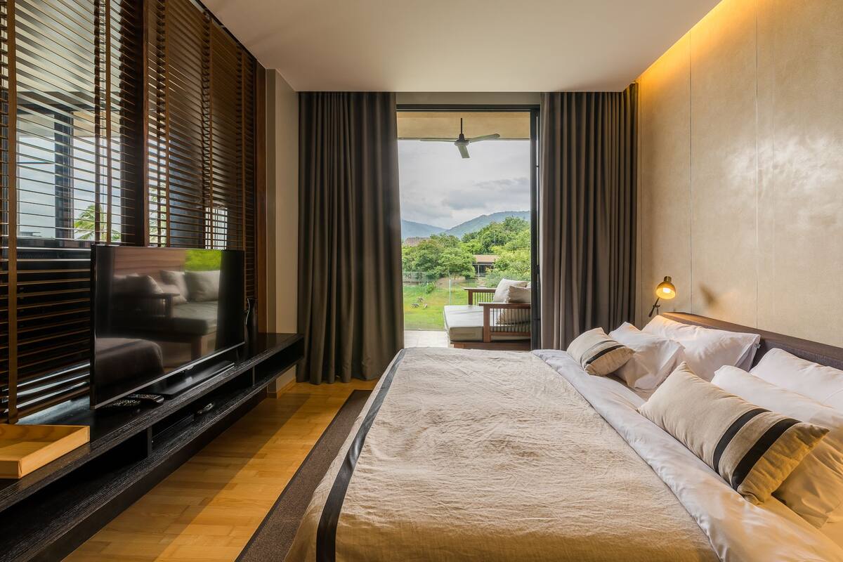 Une chambre d’hôtel moderne dotée d’un grand lit, d’une télévision à écran plat et d’un balcon offrant une vue sur la verdure et les montagnes.