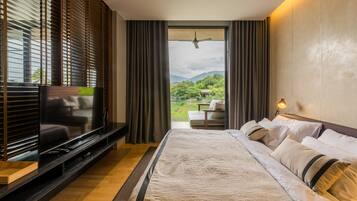 A modern hotel room with a large bed, a flat-screen TV, and a balcony with a view of greenery and mountains.