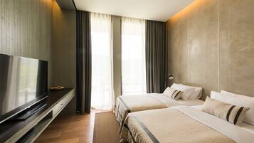 Quarto de hotel com duas camas, televisão de tela plana, piso de madeira e janelas amplas com cortinas.