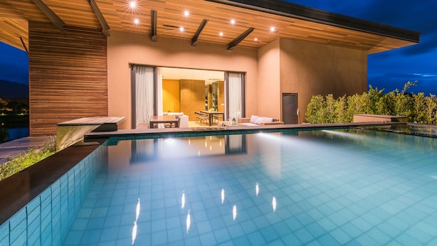 Et moderne poolområde med klart pool, træloft og siddeplads med bord og stole.