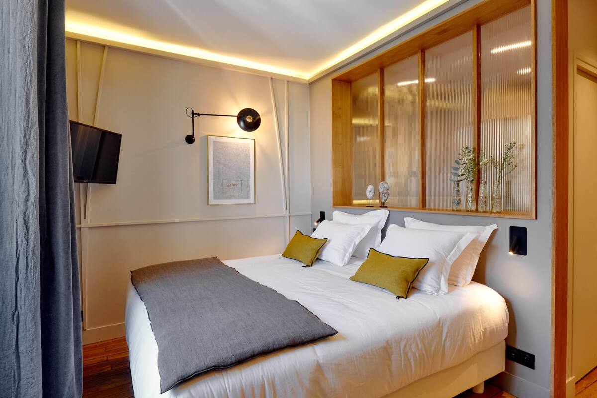 A modern bedroom with a large bed, a mounted TV, and a wall-mounted lamp.