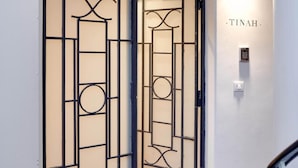 A hallway with a decorative metal gate, a wall-mounted light, and a door labeled "TINAH." - Tinah Paris - Reaumur Montorgueil (Paris)