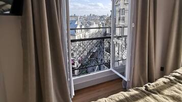 Un dormitorio con un ventanal grande, cortinas, una cama y un televisor en la pared.