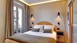 A neatly made bed with a wooden headboard, two bedside tables with lamps, and a large window with curtains. - Tinah Paris - Reaumur Montorgueil (Paris)