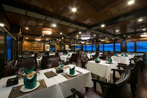 A restaurant with tables set for dining, featuring a view of the sea through large windows. - La Regina Royal Cruise (Ha Long)