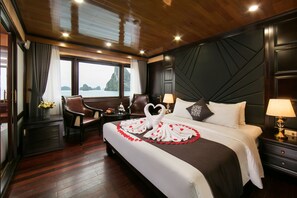 A hotel room with a large bed, a desk, a chair, and a view of the sea. - La Regina Royal Cruise (Ha Long)
