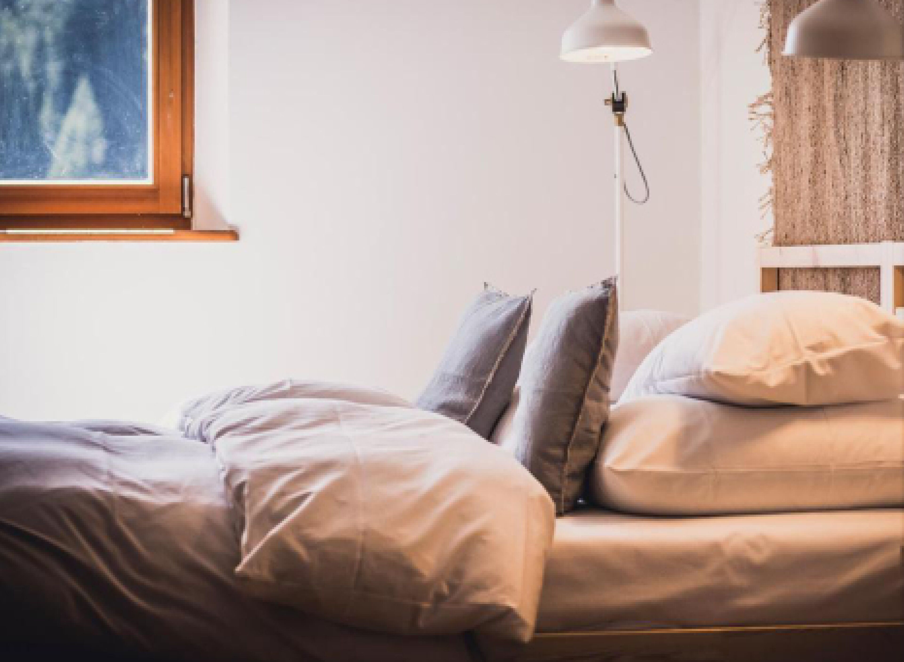 A bed with a white headboard, a bedside lamp, and a window with a view of trees.