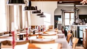 A restaurant with multiple tables and chairs, pendant lights, and a kitchen area in the background. - Berghotel Altes Wallberghaus (Rottach-Egern)