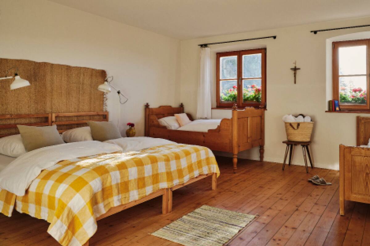 A bedroom with a wooden bed, a wooden dresser, a small table, and a window with flowers.
