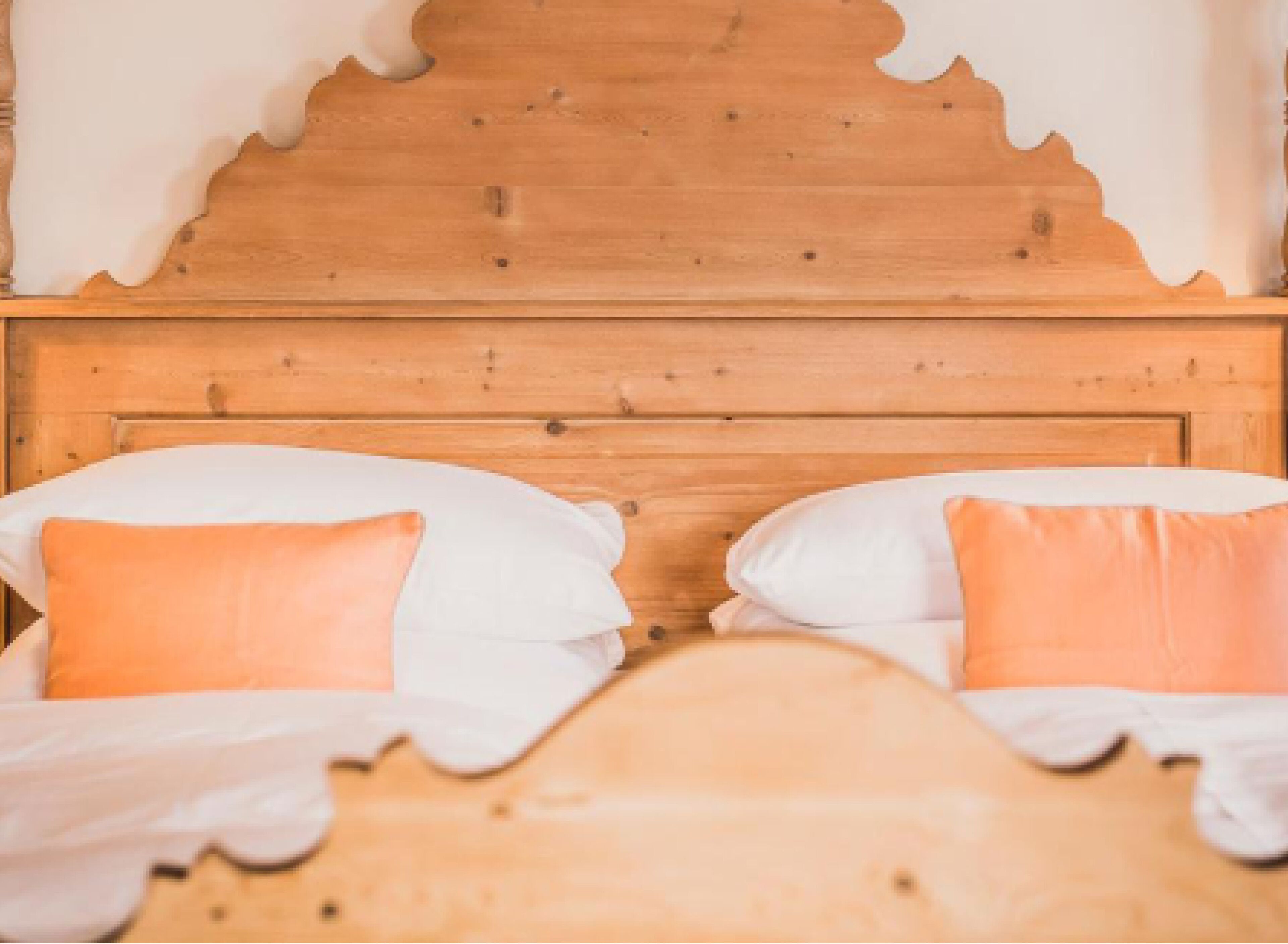 Ein Bett aus Holz mit weißen und orangefarbenen Kissen.