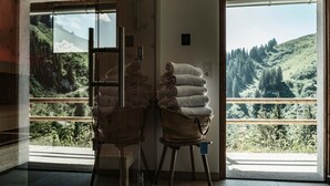A room with a large window offering a view of a green landscape. There are two wicker baskets with folded towels on a wooden stool. - Berghotel Altes Wallberghaus (Rottach-Egern)