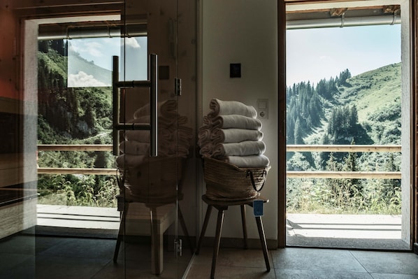 A room with a large window offering a view of a green landscape. There are two wicker baskets with folded towels on a wooden stool.
