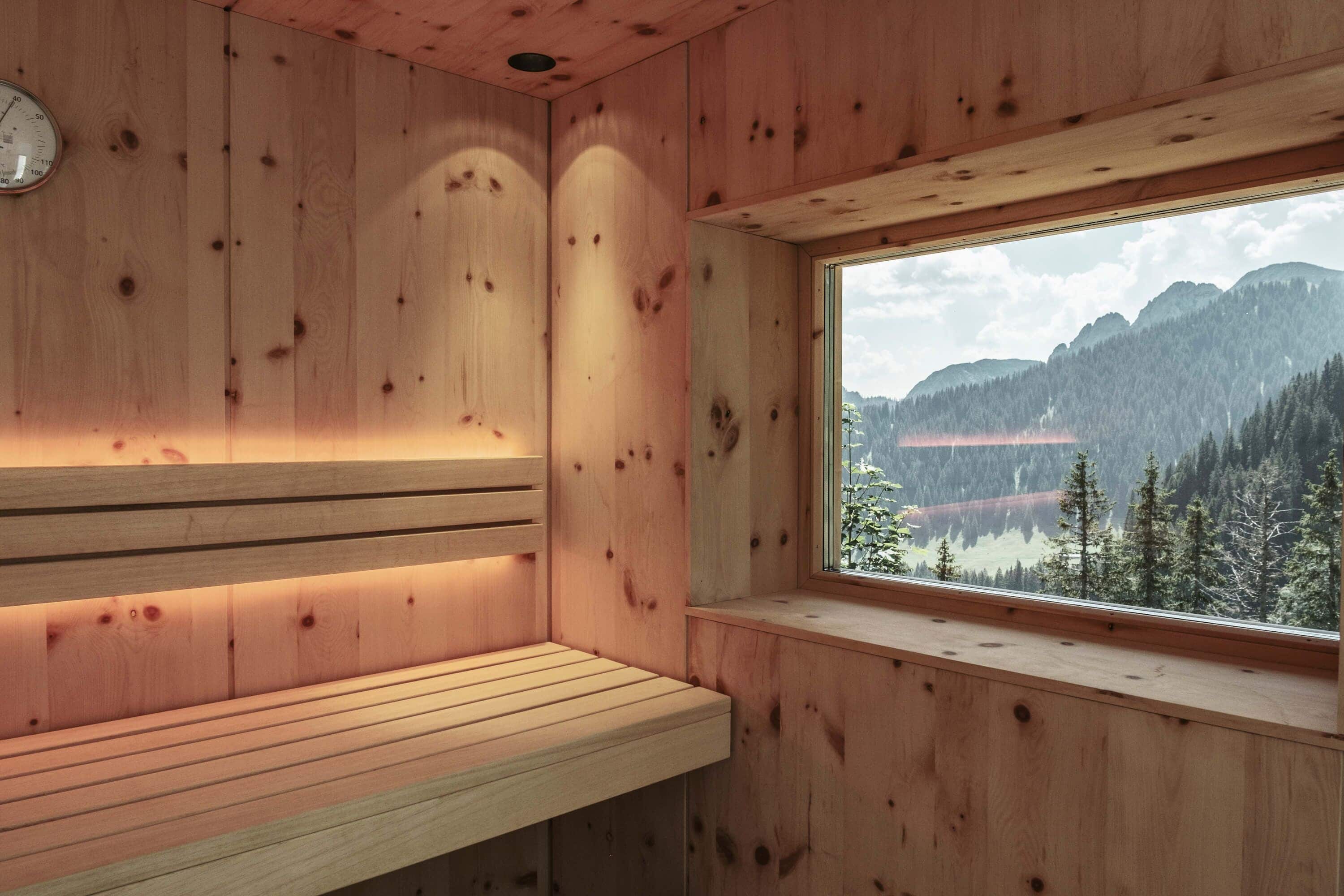 Una sauna de madera con un banco y un ventanal con vistas a la montaña.