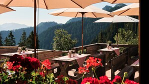 A terrace with tables and benches, surrounded by large umbrellas, overlooking a mountainous landscape. - Berghotel Altes Wallberghaus (Rottach-Egern)