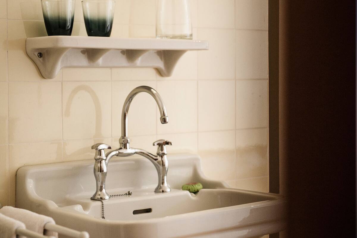 A bathroom sink with a chrome faucet, a mirror above it, and a towel rack to the left.