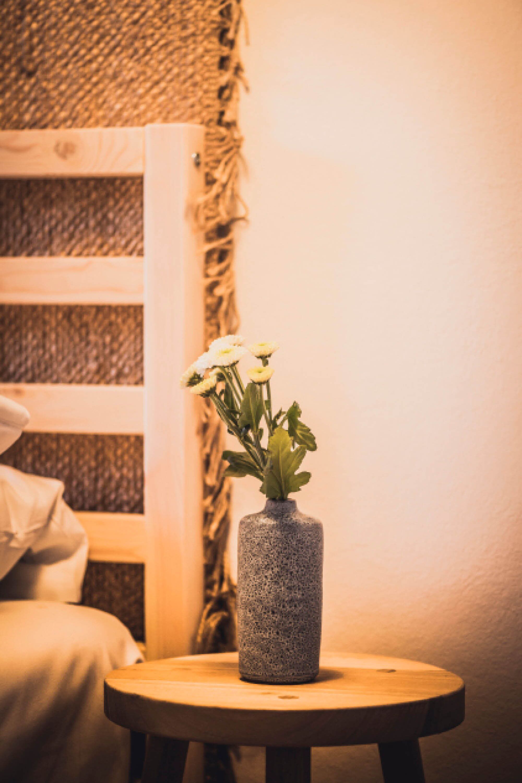 Ein runder Holztisch mit einer strukturierten Vase, gefüllt mit weißen Blumen.