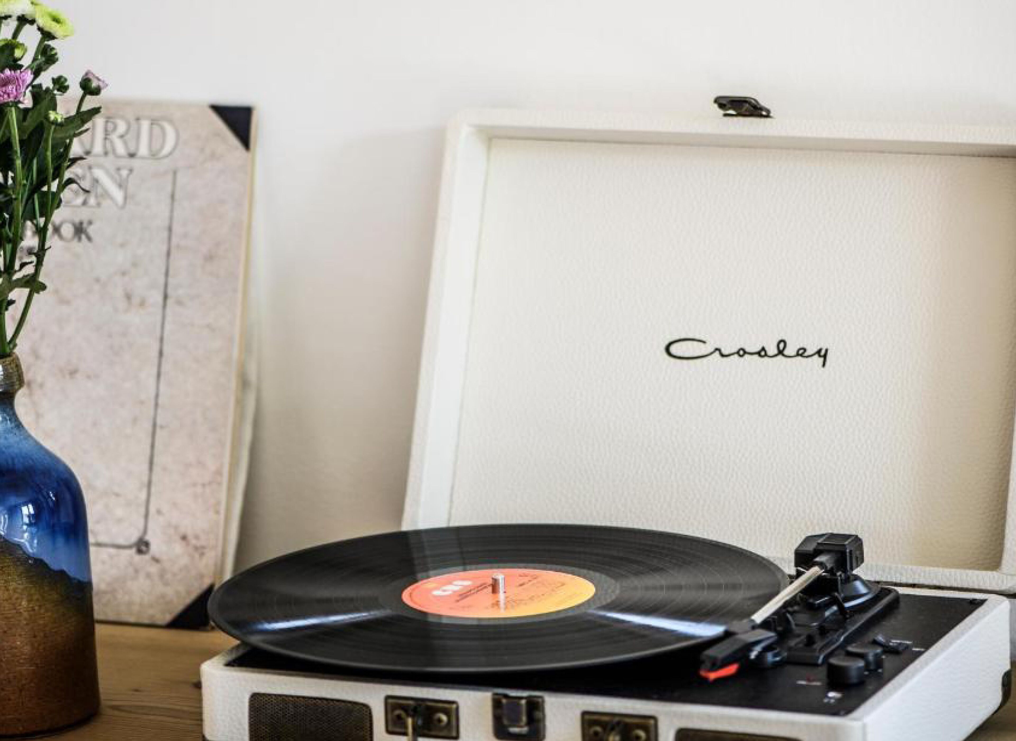 Tocadiscos de vinilo con un disco encima, un atril blanco y un jarrón con flores.