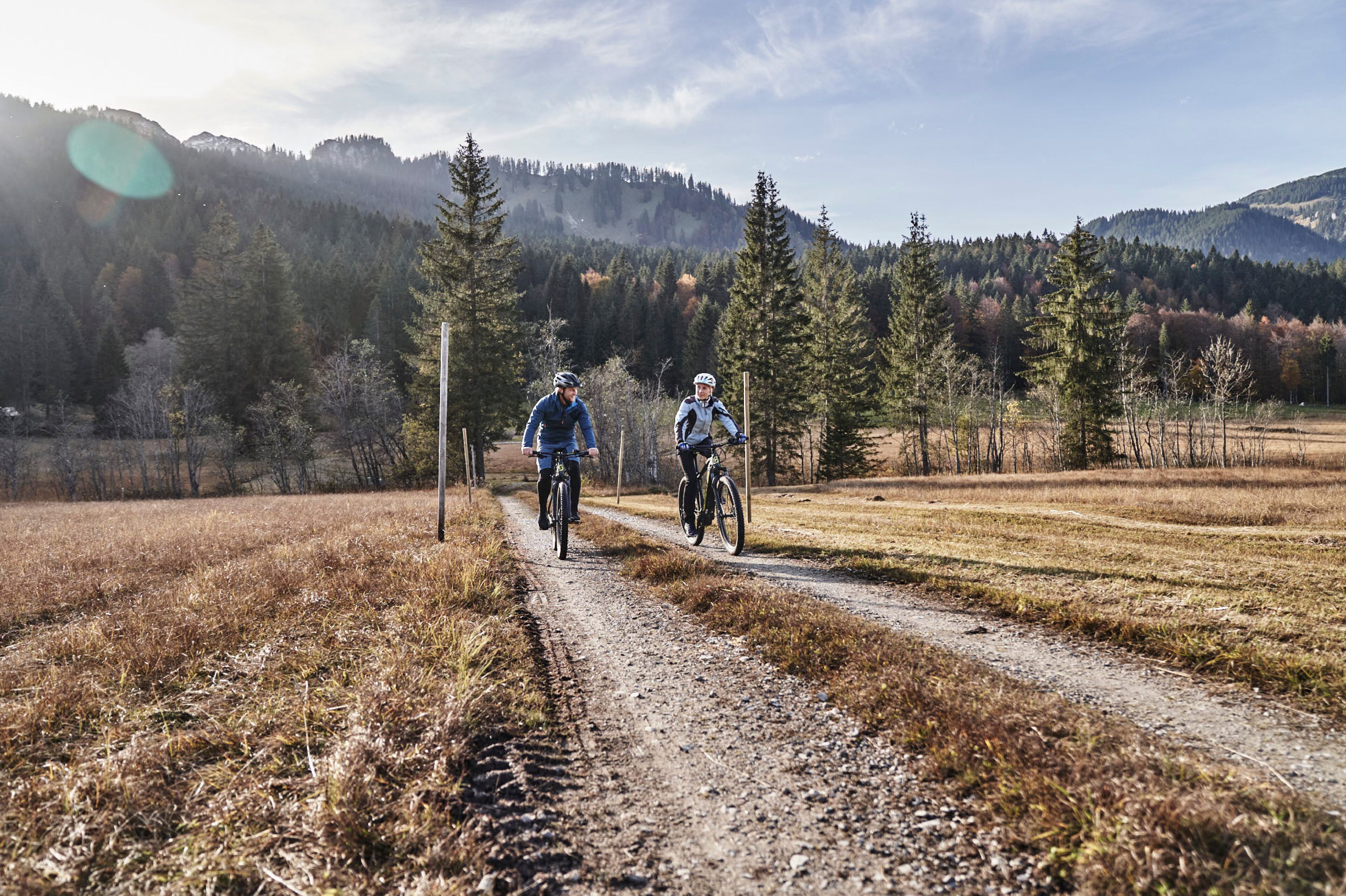 Zwei Radfahrer auf einem Feldweg, umgeben von Bäumen und Hügeln.
