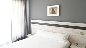 Una habitación de hotel con cama, mesita de noche, toma de corriente e imagen enmarcada en la pared.