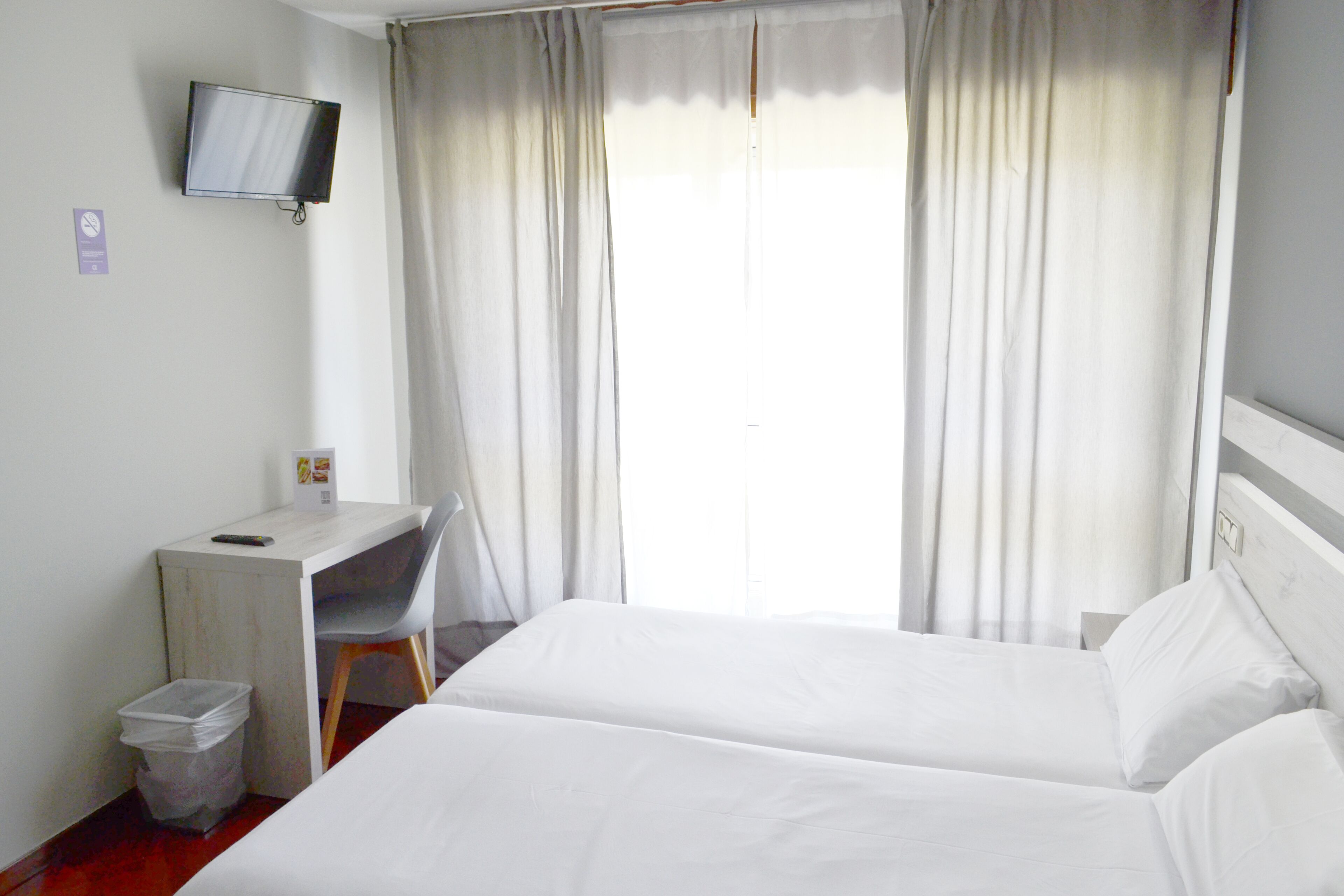 Une chambre d’hôtel avec deux lits, un bureau, une chaise, une télévision et une fenêtre avec des rideaux.