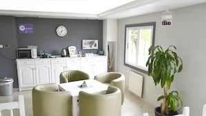 A modern kitchen with white cabinets, a microwave, and a clock on the wall. There is a dining area with a table and chairs, and a potted plant near the window. - Alda Puerta Coruña (A Coruña)