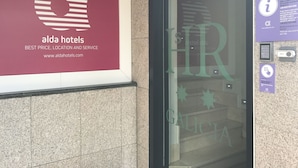 A hotel entrance with a maroon sign displaying the logo and name 'alda hotels' along with a tagline 'BEST PRICE, LOCATION AND SERVICE'. - Alda Puerta Coruña (A Coruña)