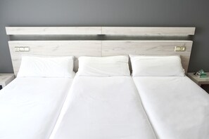 Una cama doble con sábanas blancas y cabecera de madera.