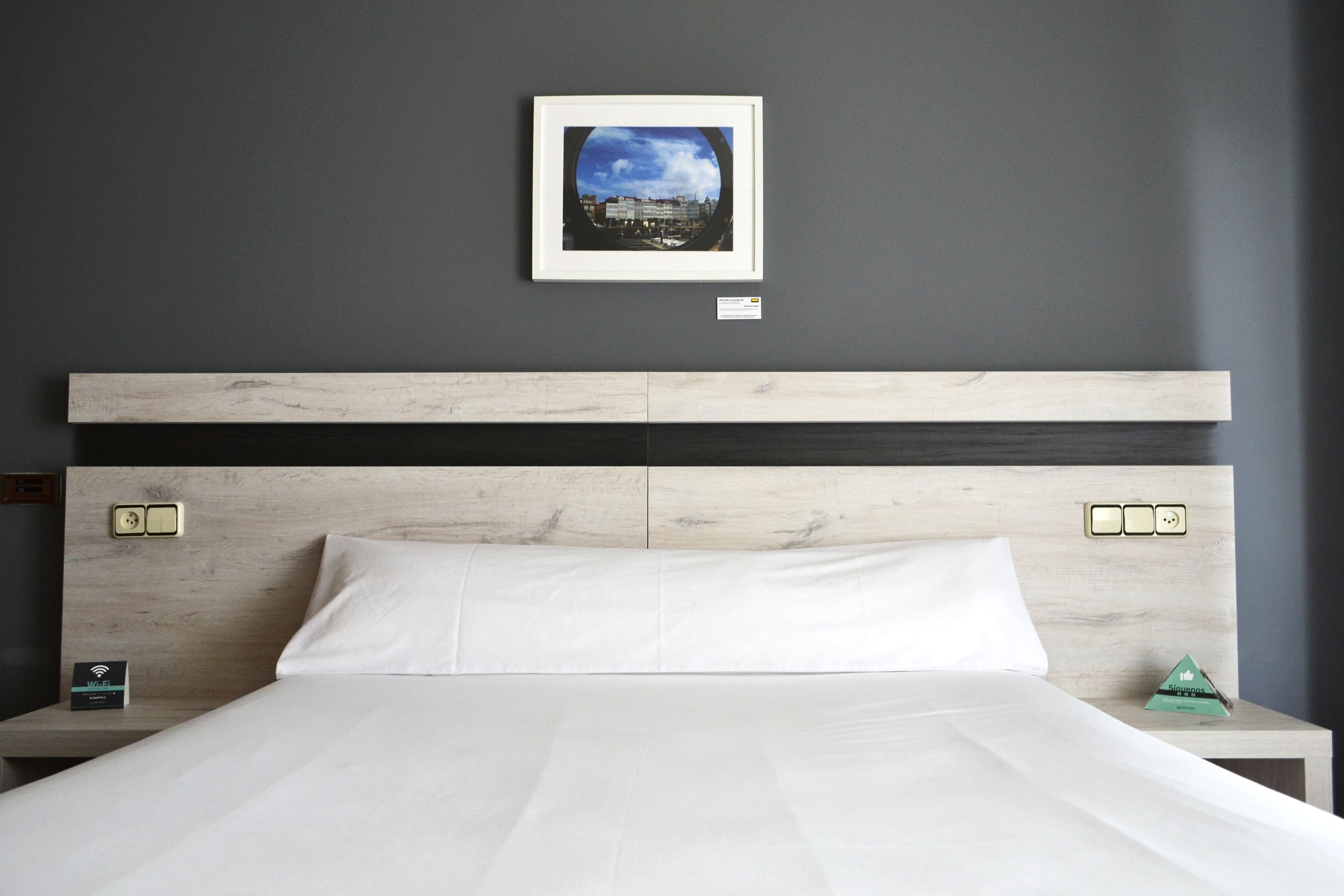A neatly made bed with white linens, a wooden headboard, and a framed picture on the wall.