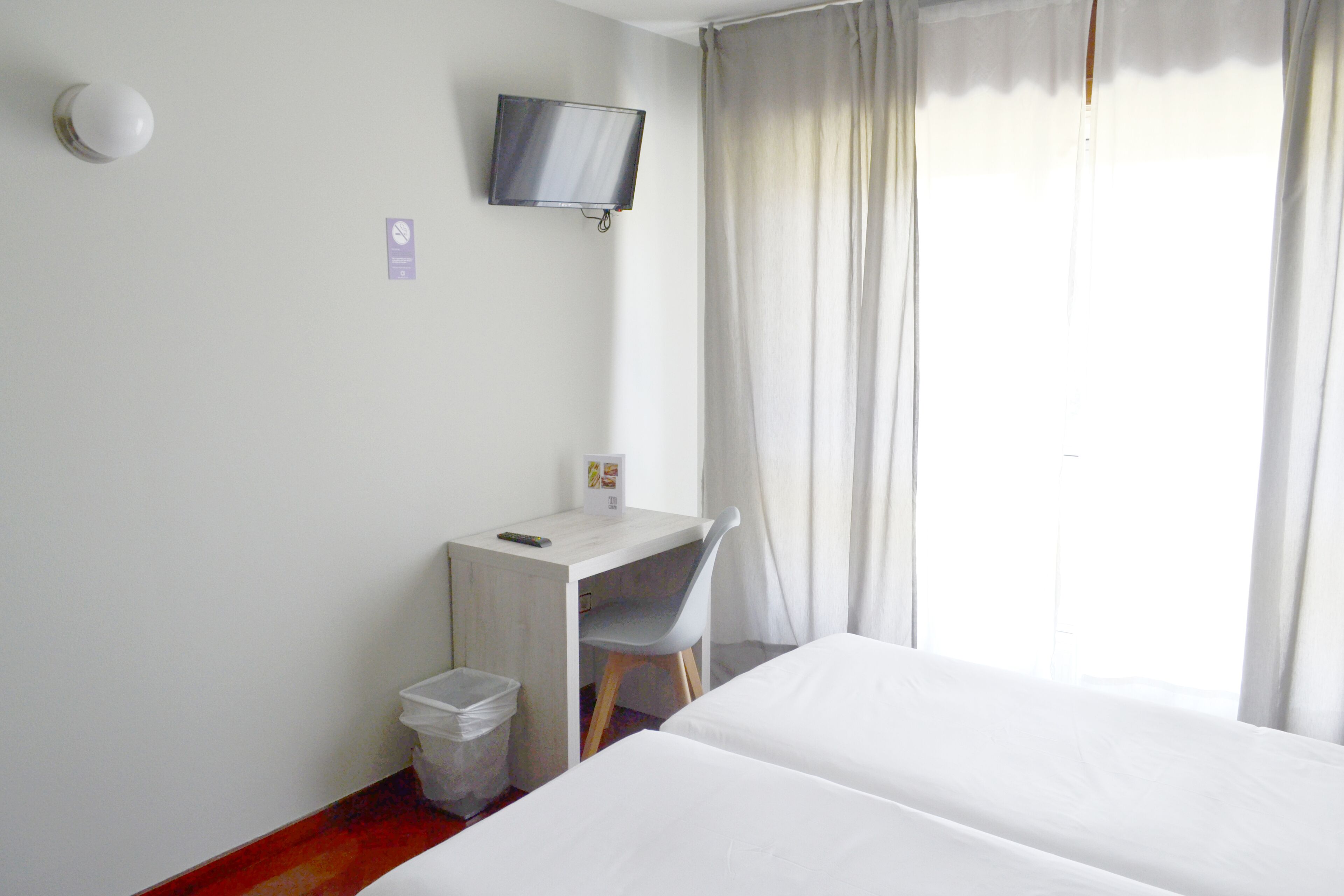 Habitación de hotel con cama, escritorio, silla, televisión y ventana con cortinas.