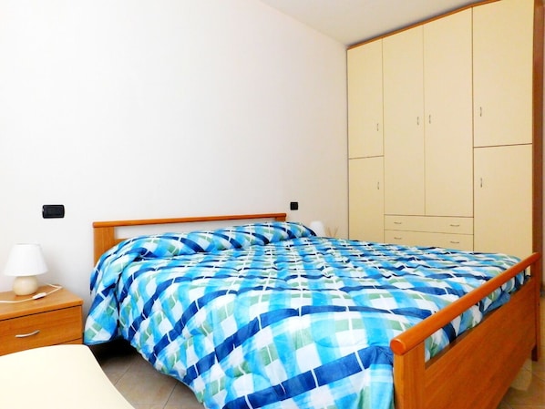 A bedroom with a bed, wooden wardrobe, bedside table, and lamp.