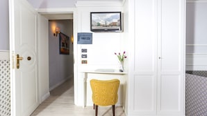 Un couloir avec une porte blanche, un bureau avec une chaise, un téléviseur fixé au mur et un vase rempli de fleurs.