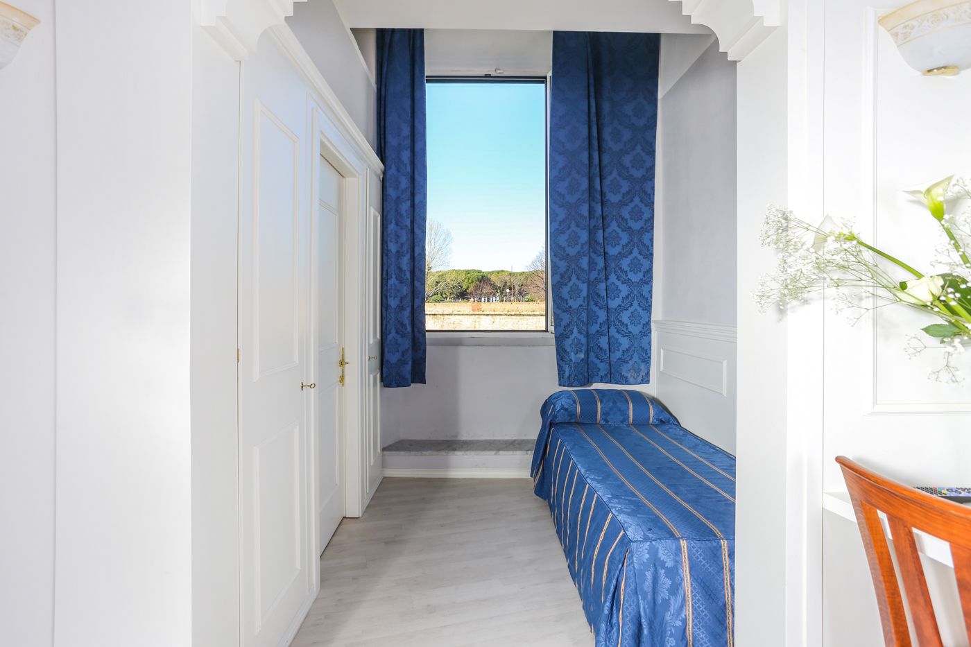 Una stanza piccola con un letto, una finestra con tende blu e vista all'esterno.