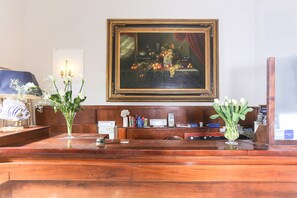 Een houten receptiebalie met daarboven een lijstwerk schilderij, een vaas met witte bloemen en een decoratie van een vis.