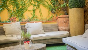 Un espace extérieur accueillant, aménagé avec des meubles en osier, une plante en pot et un mur jaune agrémenté de verdure.