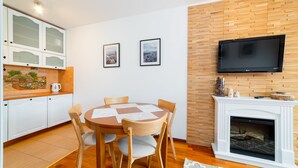 A modern kitchen with white cabinets, a dining table with chairs, a fireplace, and a mounted TV. - Apartamenty Sun & Snow Osiedle Podgórze (Szklarska Poreba)