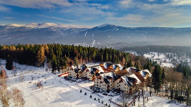 A snow-covered mountain resort with multiple chalet-style buildings, a ski slope, and a forested area. - Apartamenty Sun & Snow Osiedle Podgórze (Szklarska Poreba)