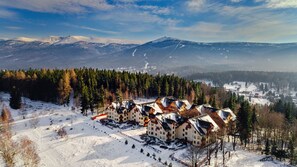 A snow-covered mountain resort with multiple chalet-style buildings, a ski slope, and a forested area. - Apartamenty Sun & Snow Osiedle Podgórze (Szklarska Poreba)