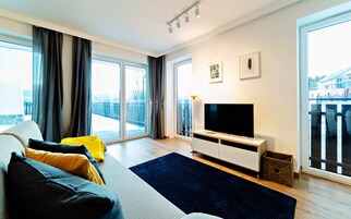 Uma sala de estar moderna com uma televis ão grande, um sofá com almofadas, um tapete escuro e uma varanda com cortinas.